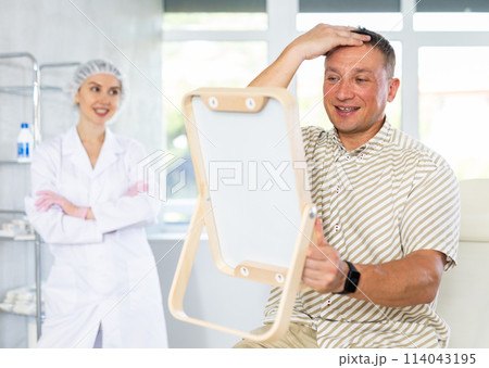 Female doctor observes results of treatment of man patient with premature hair loss Female doctor observes results of treatment of man patient with premature hair loss 114043195