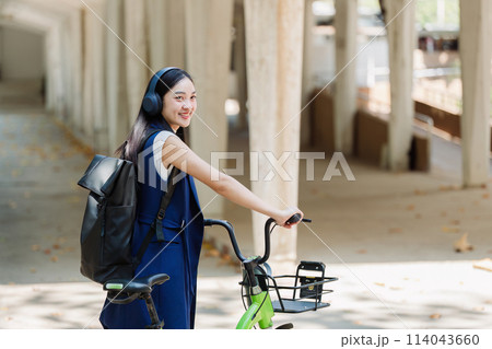 Asian young businesswoman bike to work for eco friendly green energy and listen music with headphone while commuting in city. Eco friendly Asian young businesswoman bike to work for eco friendly green energy and listen music with headphone while commuting in city. Eco friendly 114043660