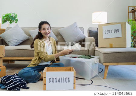 Asian young woman packing clothes at home, putting on stuff into donate box with second hand clothes Asian young woman packing clothes at home, putting on stuff into donate box with second hand clothes 114043662