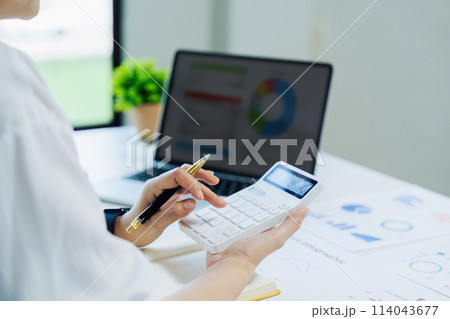 Businesswoman using a calculator to calculate numbers on a company's financial documents, she is analyzing historical financial data to plan how to grow the company. Financial concept 114043677
