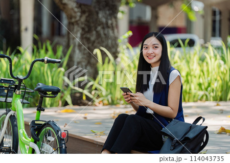asian young businesswoman use smart phone while commuting in city. Eco friendly asian young businesswoman use smart phone while commuting in city. Eco friendly 114043735