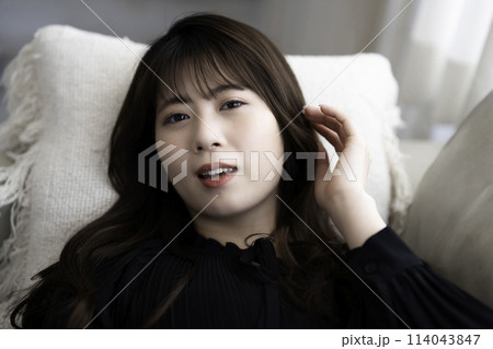 ソファに寝転んでくつろぐ若い女性 114043847