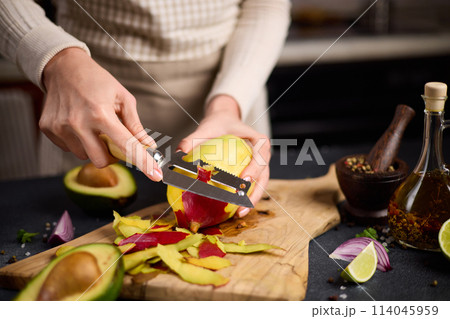 Woman peeling mango on a wooden cutting board at domestic kitchen 114045959