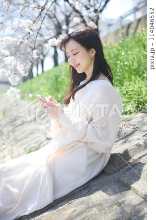 桜の下でスマホを見る女性 114046552
