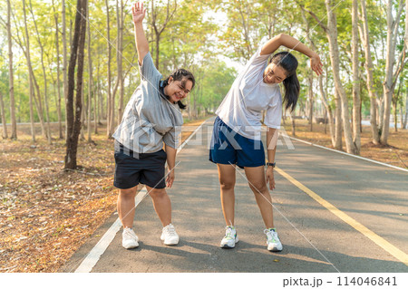 Two young female friends stretching their arms and legs before starting their morning run at a local running park 114046841