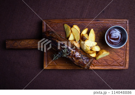 top view of the beef steak with baked potato wedges and rosemary on a wooden board 114048886