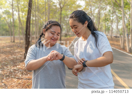Two young female friends checking out their run time on their smart watch after their morning run at a local running park 114050713