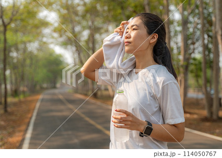 Young woman wiping off her sweat after her morning run at a local running park 114050767