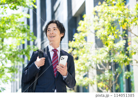 スマホを持ってスーツ姿で歩くビジネスマン スマホを持ってスーツ姿で歩くビジネスマン 114051385