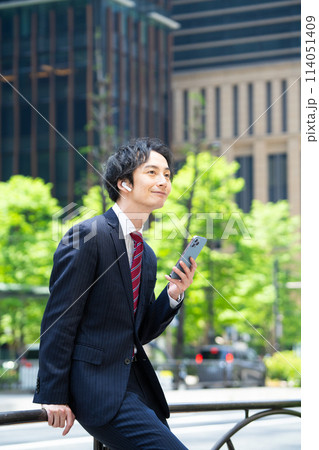 ワイヤレスイヤホンをしてスマホを使うビジネスマン ワイヤレスイヤホンをしてスマホを使うビジネスマン 114051409