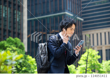 ワイヤレスイヤホンをしてスマホを使うビジネスマン ワイヤレスイヤホンをしてスマホを使うビジネスマン 114051411