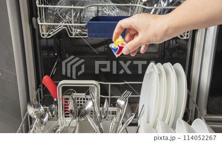 Woman putting detergen kapsul into open dishwasher Woman putting detergen kapsul into open dishwasher 114052267