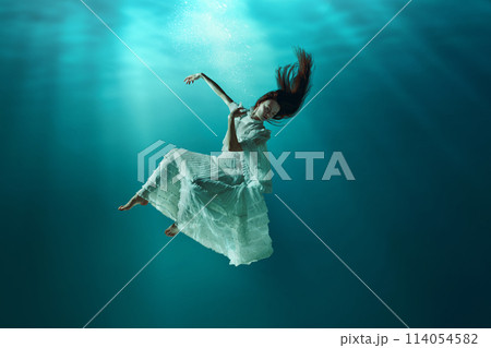 Amazing aquatic scene of elegant young girl lightly floating in the ocean, ocean with sunlight on surface. Diving in mysterious world 114054582