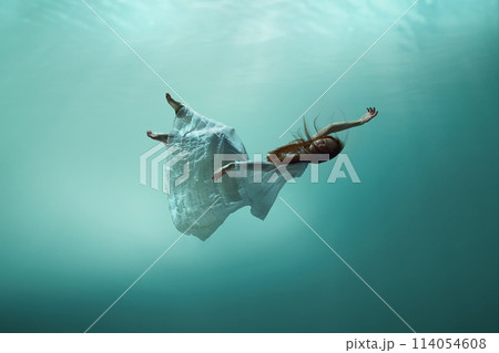 Magic and mystery hidden beneath the ocean. Elegant young girl levitating underwater, finding peace and calmness 114054608
