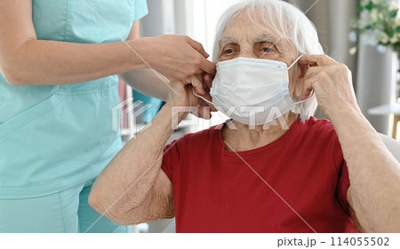 Nurse Helps Elderly Woman Put On Medical Protective Mask During Period Of Viral And Respiratory Diseases 114055502