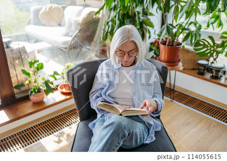 Beautiful mature woman reading book, feeling cozy and happy. Weekend activity for older woman, relaxing at home. 114055615