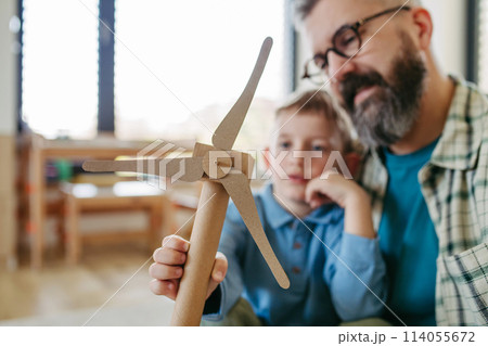 Son and father holding wind turbine model. Concpet of renewable energy sustainable lifestyle for next generations. 114055672