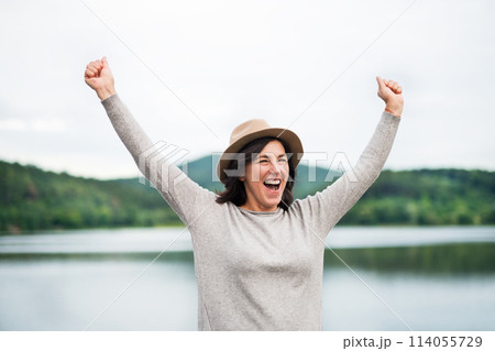 Portrait of beautiful mature woman with hat on vacation. Hands in the air, happiness. 114055729