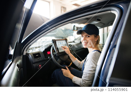 Female auto mechanic using diagnostic tool, scanner, running diagnostic on car. Beautiful woman sitting inside of car, performing diagnostic test. Female auto mechanic using diagnostic tool, scanner, running diagnostic on car. Beautiful woman sitting inside of car, performing diagnostic test. 114055901