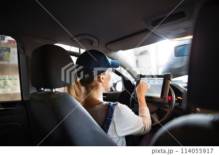 Female auto mechanic using diagnostic tool, scanner, running diagnostic on car. Beautiful woman sitting inside of car, performing diagnostic test. 114055917