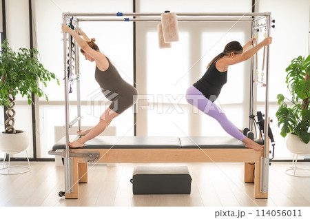 Two pregnant women are doing Pilates on a Cadillac reformer. Two pregnant women are doing Pilates on a Cadillac reformer. 114056011
