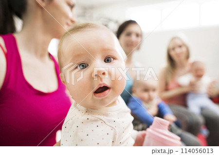 Baby movement class. Parents helping babies to improve motor skills, proper movement on fitball. Pediatric physical therapist leading class. Mothers exercising with babies. 114056013