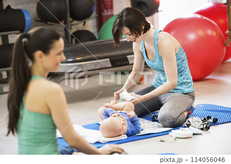 Mother changing diaper during group exercise class. Moms staying active, working out with baby in gym, bonding. Mother changing diaper during group exercise class. Moms staying active, working out with baby in gym, bonding. 114056046