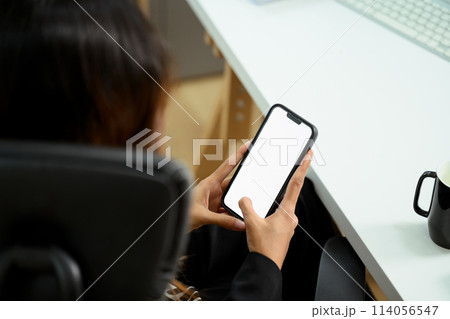 Close up businesswoman holding smartphone with blank screen sitting at her workplace 114056547