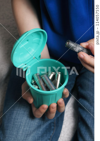 Teenager's hand dropping used batteries into a small waste container, illustrating the need for proper disposal and eco-friendly habits. Recycling concept. 114057550