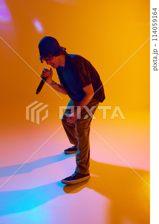 Dynamic performance. Young musician delivers dynamic rap, captivating the audience with creative art against yellow background in neon light Dynamic performance. Young musician delivers dynamic rap, captivating the audience with creative art against yellow background in neon light 114059164