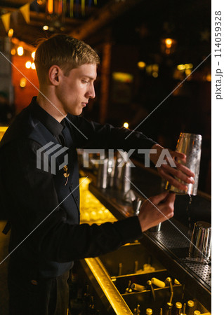Barman uses strainer to sieve large pieces of ice from shaker 114059328