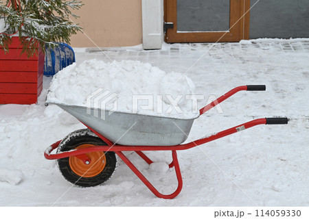 Metal wheelbarrow with dirty snow, street cleaning. Snow removal in city, construction works, urban landscaping in winter 114059330