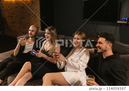 Laughing young women sit amidst men playing console games Laughing young women sit amidst men playing console games 114059397