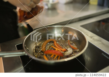 Cook in gloves holds pack with spices frying vegetables 114059422