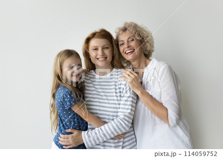 Beautiful multi-generational relatives women hugging posing on gray studio background 114059752