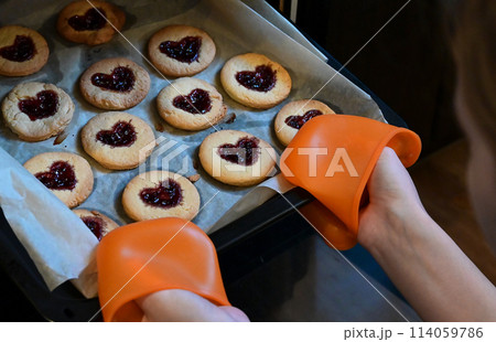 Woman is putting a baking sheet with delicious homemade cookies in the shape of a heart in the oven. Concept of fresh homemade cakes or a surprise for Valentine's Day, Mothers day. Woman is putting a baking sheet with delicious homemade cookies in the shape of a heart in the oven. Concept of fresh homemade cakes or a surprise for Valentine's Day, Mothers day. 114059786