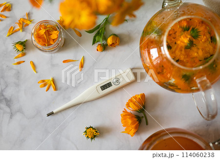 Cup of marigold tea and calendula flowers outdoors on green background. 114060238