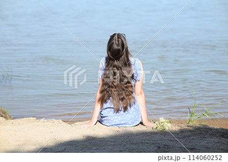 A young girl with long dark hair stands on the bank of the river. 114060252