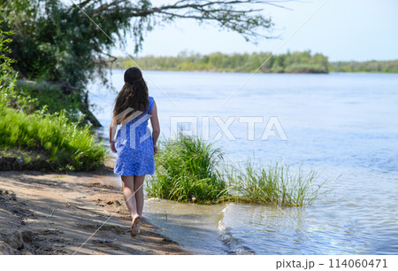 A young girl with long dark hair stands on the bank of the river. A young girl with long dark hair stands on the bank of the river. 114060471