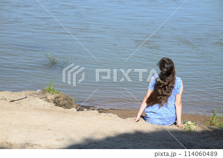 A young girl with long dark hair stands on the bank of the river. 114060489
