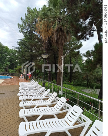 The deck chairs are empty, standing in a row, near the pool. The deck chairs are empty, standing in a row, near the pool. 114060841