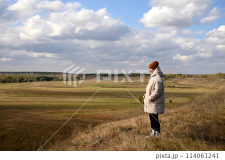 A girl in a light jacket and a brown hat looks at the autumn landscape A girl in a light jacket and a brown hat looks at the autumn landscape 114061241