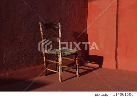 Old wooden one vintage chair in a room with red grunge walls and floor in sunlight, dark shadows. Shabby antique furniture. Empty copy space, no people. Retro interior still life, concept. 114061506