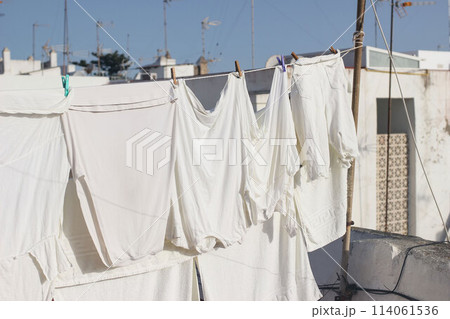 White various clothes hanging and drying in wind on rope. Laundry with clothes pins on line outdoors. Spanish rooftop. Summer Mediterranean still life, city life. No people. 114061536