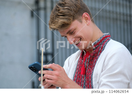 masterfully play drum beautiful young guy of European appearance in Ukrainian embroidered shirt national clothes of Ukraine plays drum waving sticks power of happiness professional musician fast play 114062654
