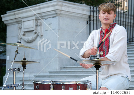 masterfully play drum beautiful young guy of European appearance in Ukrainian embroidered shirt national clothes of Ukraine plays drum waving sticks power of happiness professional musician fast play 114062685