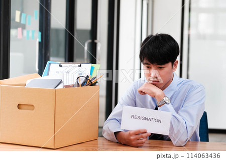 Man at desk with resignation letter, pondering his decision beside a packed box. 114063436