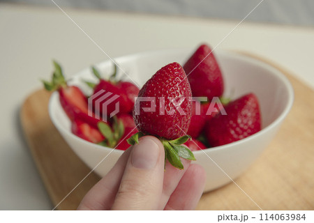 Close-up of strawberries in a woman hands against the background of strawberries in a bowl Close-up of strawberries in a woman hands against the background of strawberries in a bowl 114063984