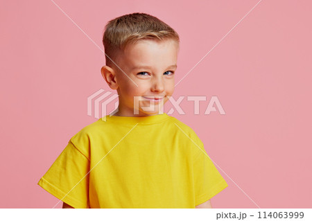 Portrait of little boy with sly expression looking at the camera against pink studio background. Cheating on lessons. 114063999