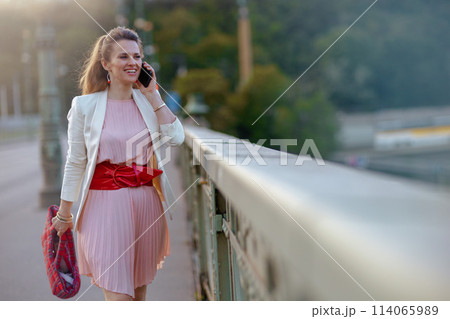 smiling woman in dress and jacket in city using phone smiling woman in dress and jacket in city using phone 114065989